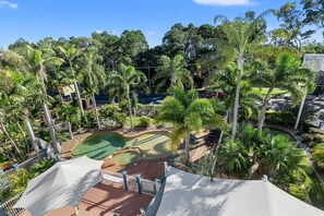 Vista de un campo de golf con un putting green, rodeado de palmeras y una estructura similar a una carpa blanca.