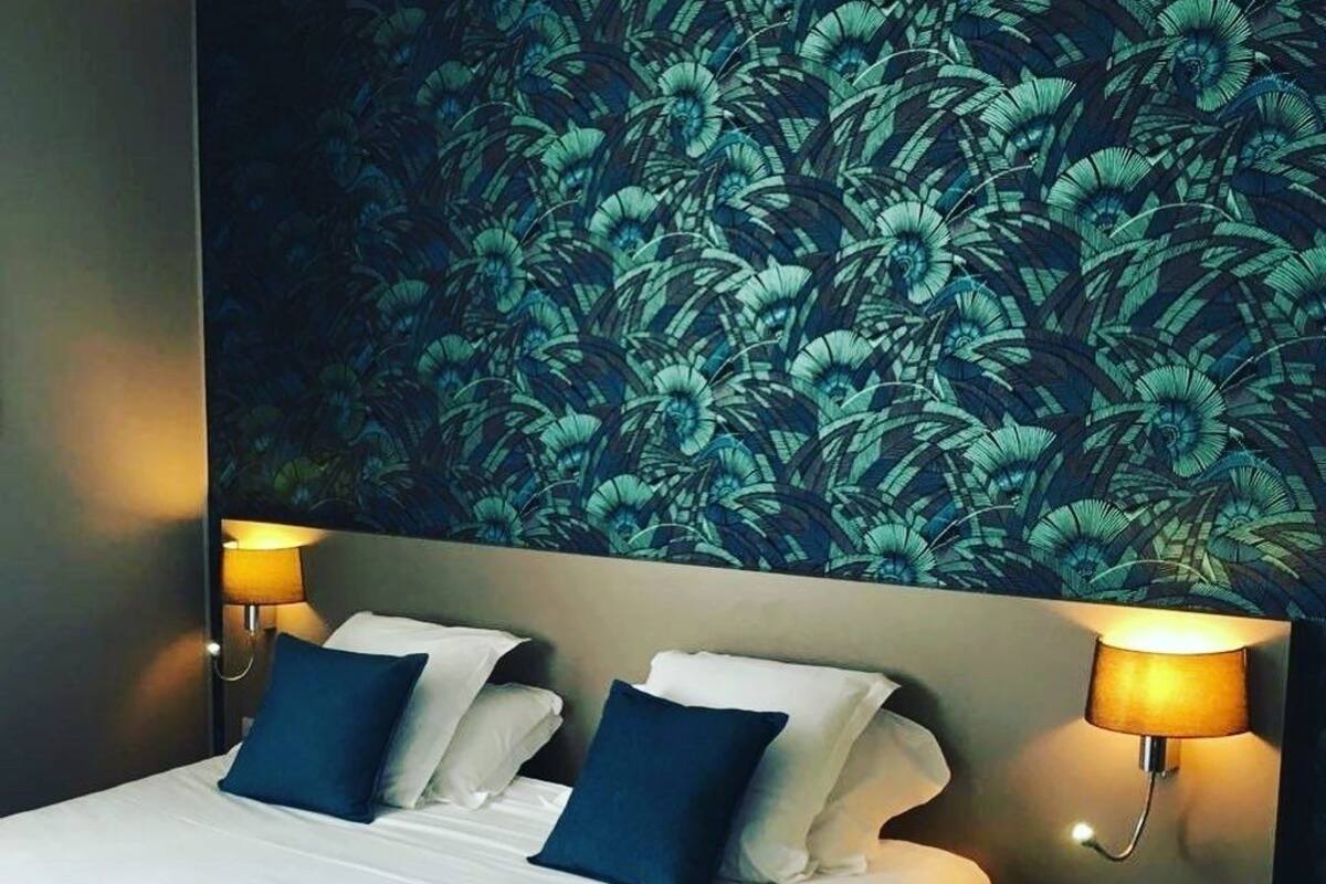 Une chambre d’hôtel avec un lit, deux lampes de chevet et un papier peint à motifs floraux.