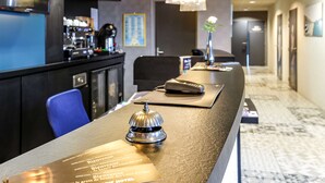 Zona de recepción de un hotel con barra, mostrador de recepción y pasillo que da a las habitaciones.