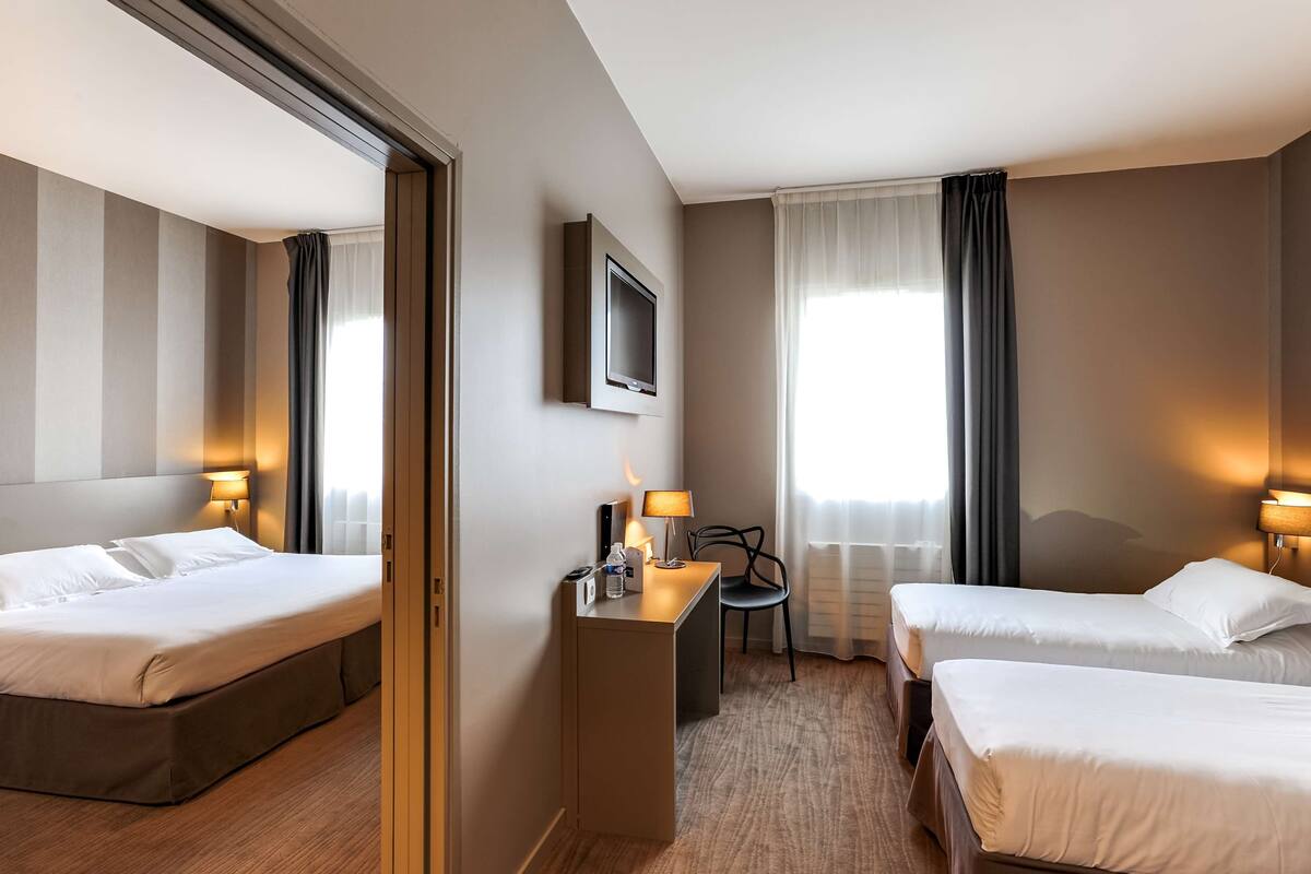 Une chambre d’hôtel avec deux lits, un bureau avec une lampe, une télévision et une chaise.