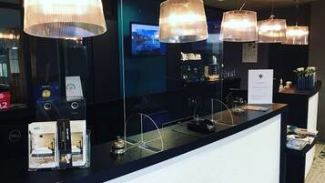 A hotel reception area with a black counter, multiple pendant lights, a digital screen, and a reception desk.