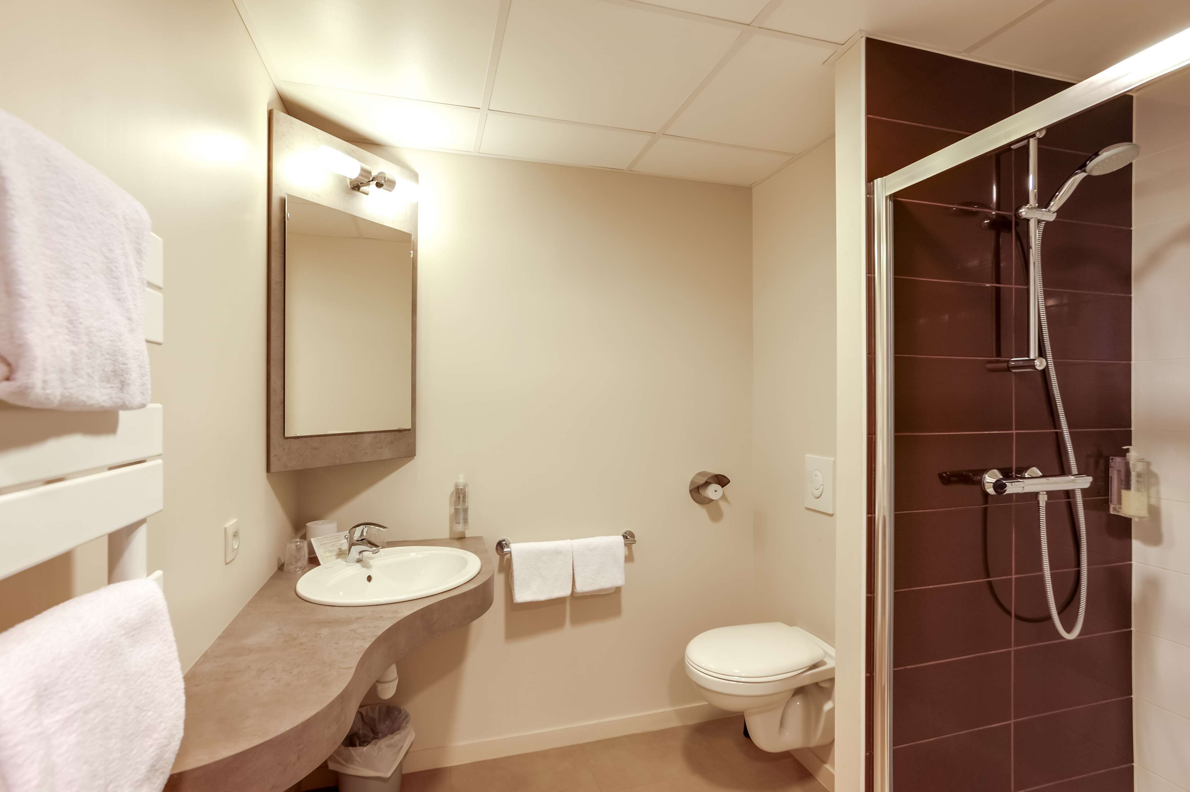 A bathroom with a sink, mirror, towel rack, toilet, and shower.