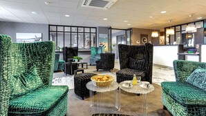 Un vestíbulo con sillones tapizados en verde, un mostrador de recepción y un ventanal grande.