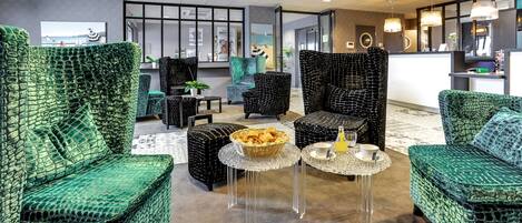 A lobby with green upholstered chairs, a reception desk, and a large window.