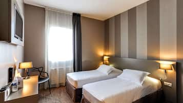 Habitación de hotel con dos camas, un escritorio con lámpara, una silla y un televisor en la pared.