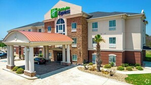 A Holiday Inn Express hotel with a covered entrance, a parking lot, and a landscaped area with palm trees. - Holiday Inn Express Kenedy by IHG (Kenedy)