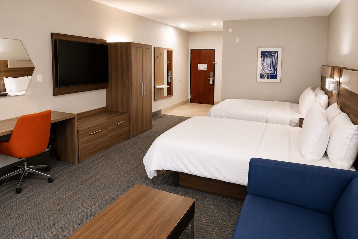 A hotel room with a bed, a desk, a chair, a TV, and a door.