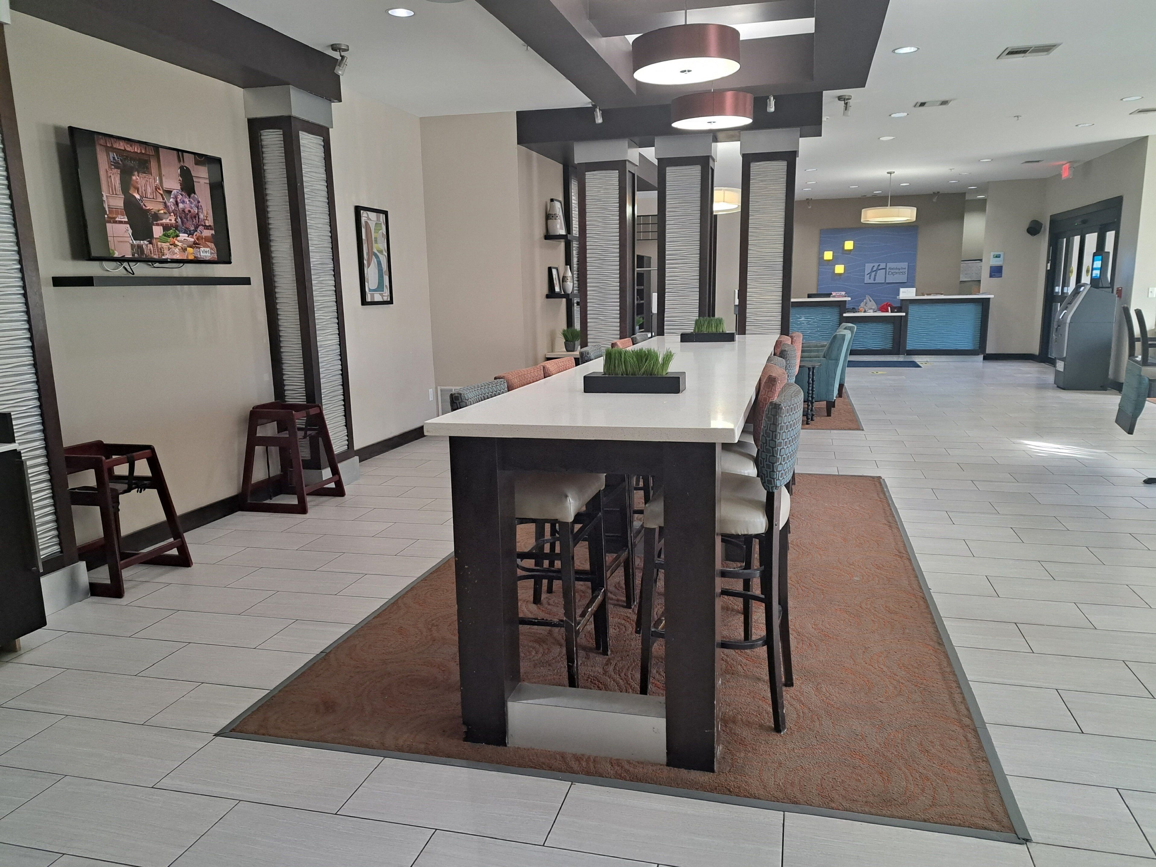 A modern hotel lobby with a long dining table, seating, and a reception area.