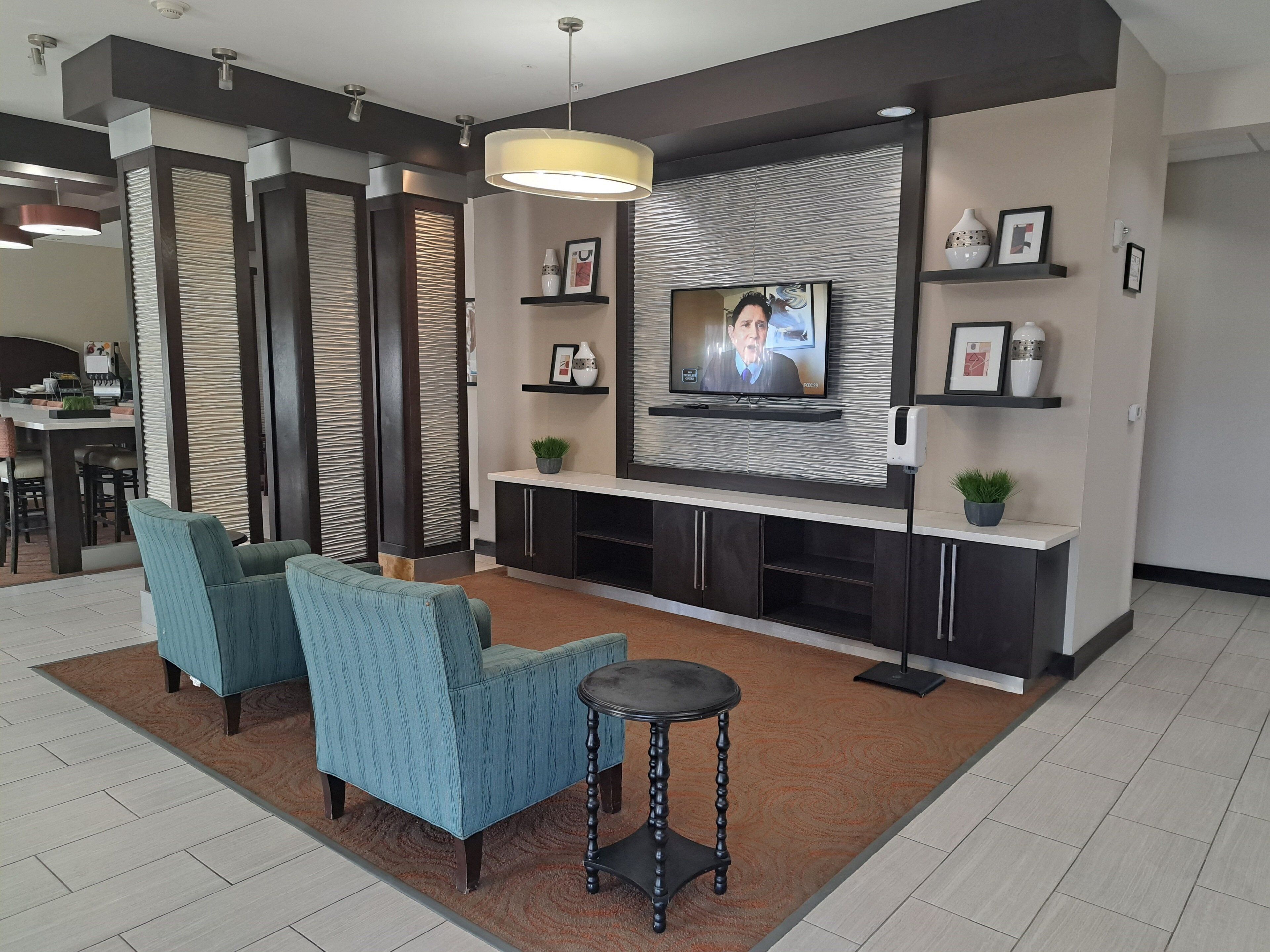 A modern living room with a flat-screen TV, two blue armchairs, a coffee table, and a fireplace.