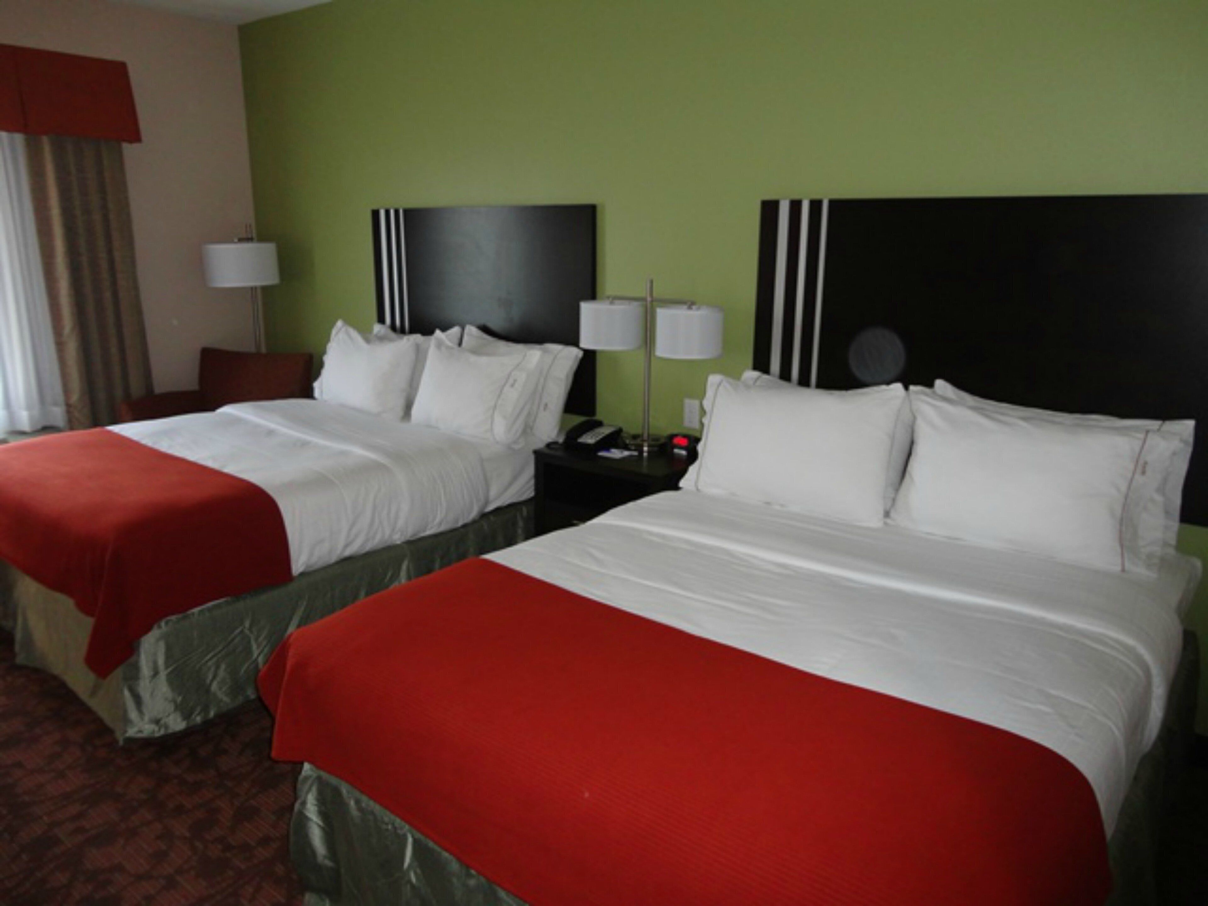 Une chambre d’hôtel avec deux lits, chacun étant équipé de draps blancs et d’une couverture rouge. Il y a des tables de chevet avec des lampes et une horloge. Les murs sont peints en vert.