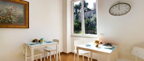 Un comedor con una mesa y sillas, un reloj en la pared y una ventana con vistas a follaje.