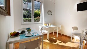 Een eethoek met een tafel gedekt voor twee personen, een klok aan de muur en een raam met uitzicht op groen.