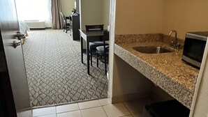 A compact hotel room with a kitchenette, a dining area with a table and chairs, and a bathroom with a sink and toilet.