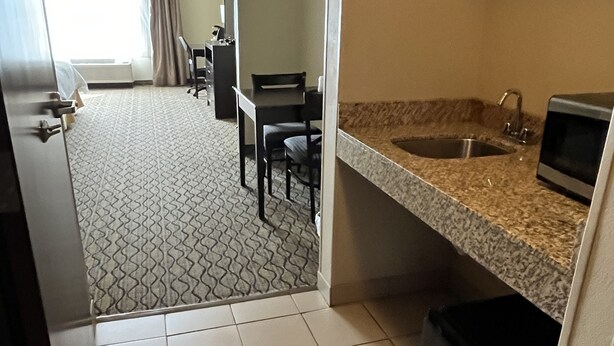 Een compacte hotelkamer met een kitchenette, een zithoek met tafel en stoelen, en een badkamer met wastafel en toilet.