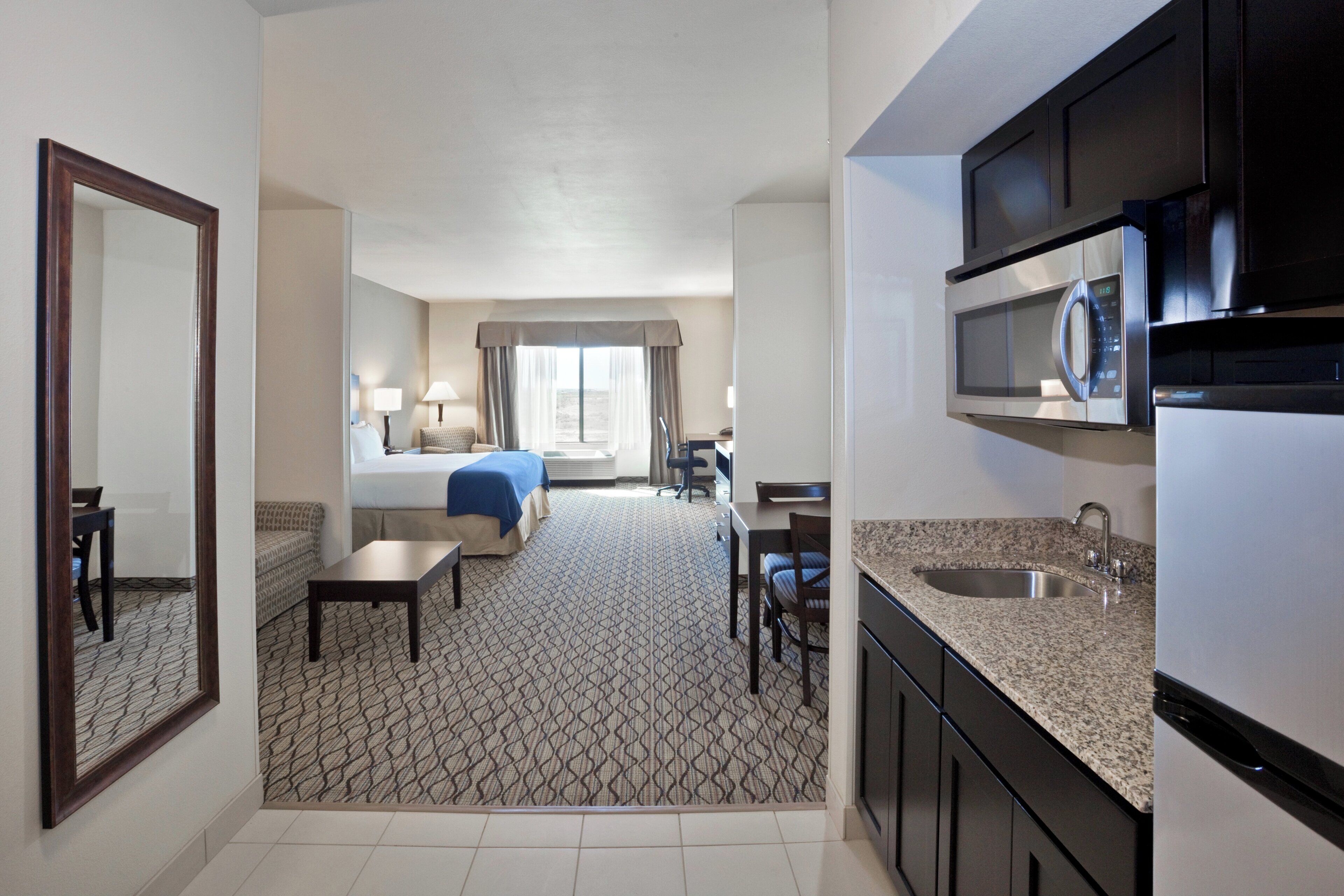 Habitación de hotel con kitchenette, una cama, un escritorio y un comedor.
