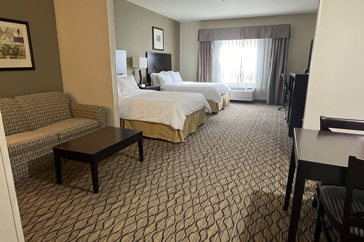 A hotel room with a patterned carpet, two beds, a sofa, a small table, and a TV.