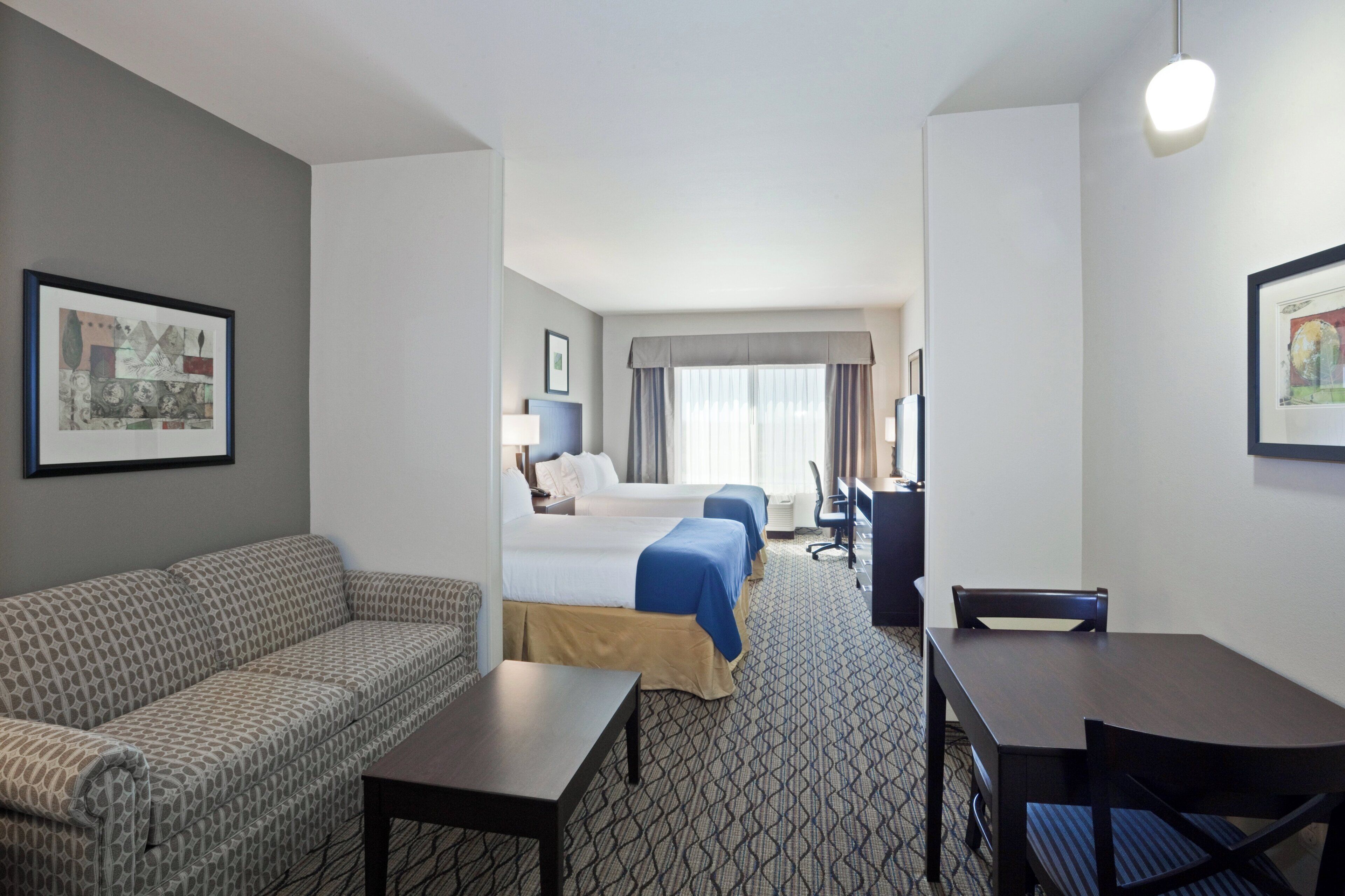 A hotel room with a sofa, two beds, a desk, and a chair.