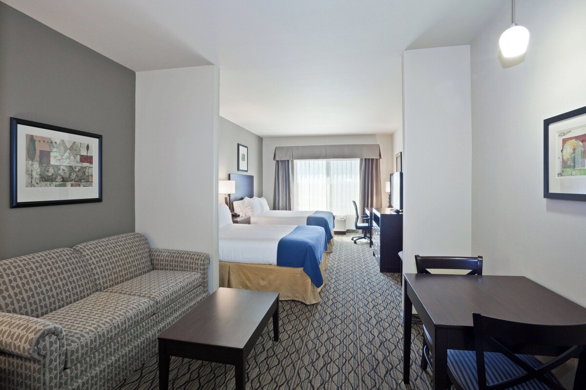 A hotel room with a sofa, two beds, a desk, and a chair.