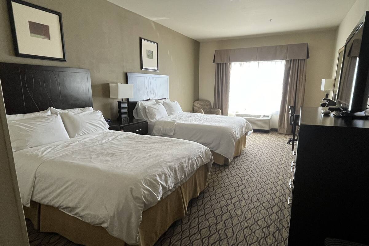 A hotel room with two beds, a desk, a chair, a TV, and a window with curtains.