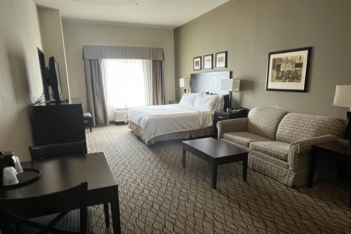A hotel room with a bed, a sofa, a desk, and a TV.