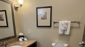 Een badkamer met een wastafel, spiegel, fotolijst, toilet en handdoekrek.