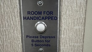 Een bord dat een kamer voor mensen met een handicap aangeeft, met een knop die 5 seconden ingedrukt kan worden.
