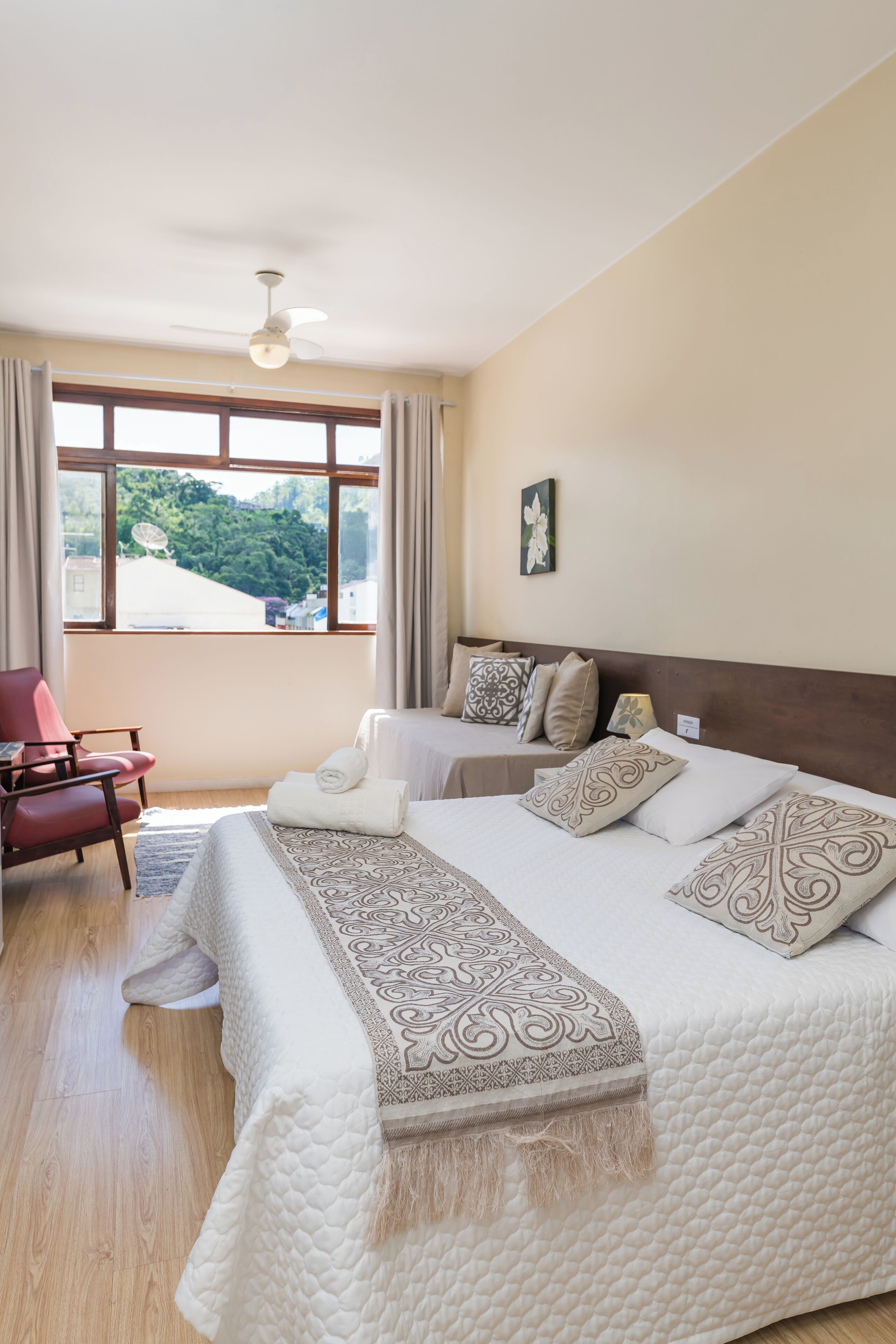 Un dormitorio con una cama grande, una silla, un escritorio y vistas a un paisaje verde a través de la ventana.