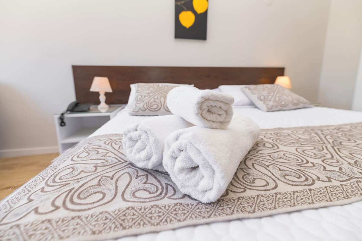A neatly made bed with rolled towels, patterned pillows, and a bedside lamp.
