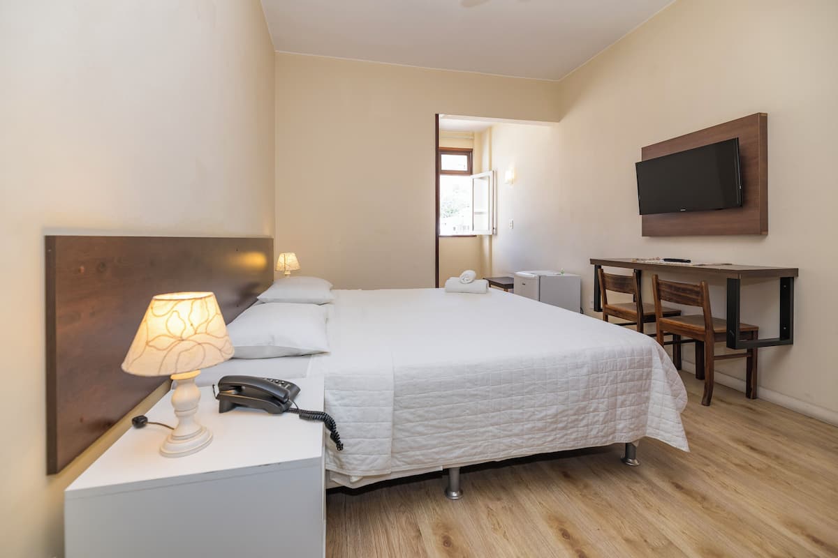 A hotel room with a bed, bedside lamp, telephone, and a TV mounted on the wall.