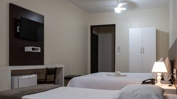 A hotel room with two beds, a desk with a flat-screen TV, a wardrobe, and a bedside lamp.