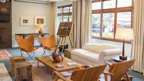 Una sala de estar con un sofá, dos sillones, una mesita de centro, un cuadro sobre caballete y un televisor.
