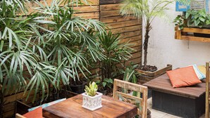 Un patio de madera con una mesa y sillas, rodeado de macetas con plantas y una pared con paneles de madera.