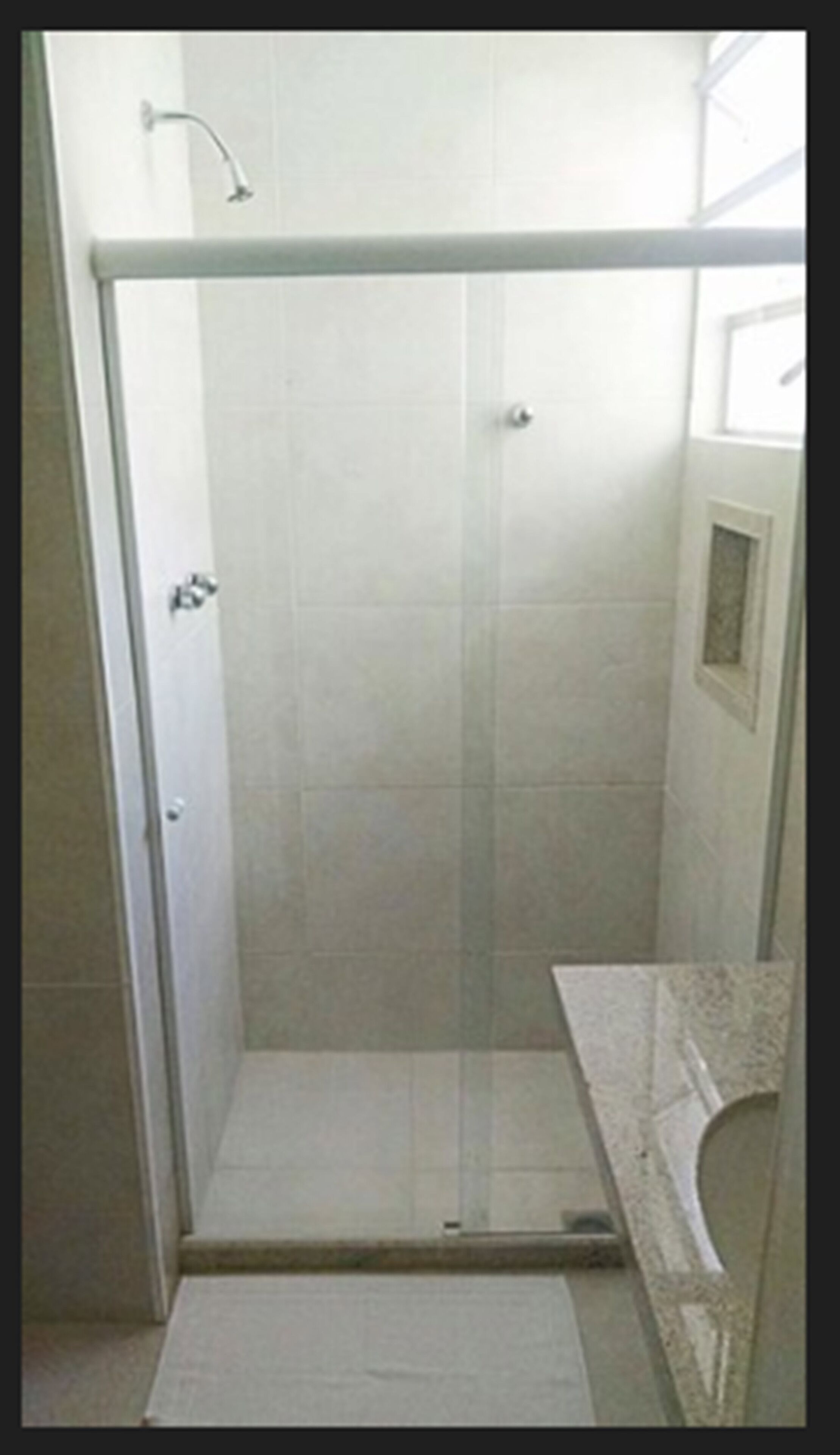 A glass-enclosed shower stall with a tiled floor and a small window.