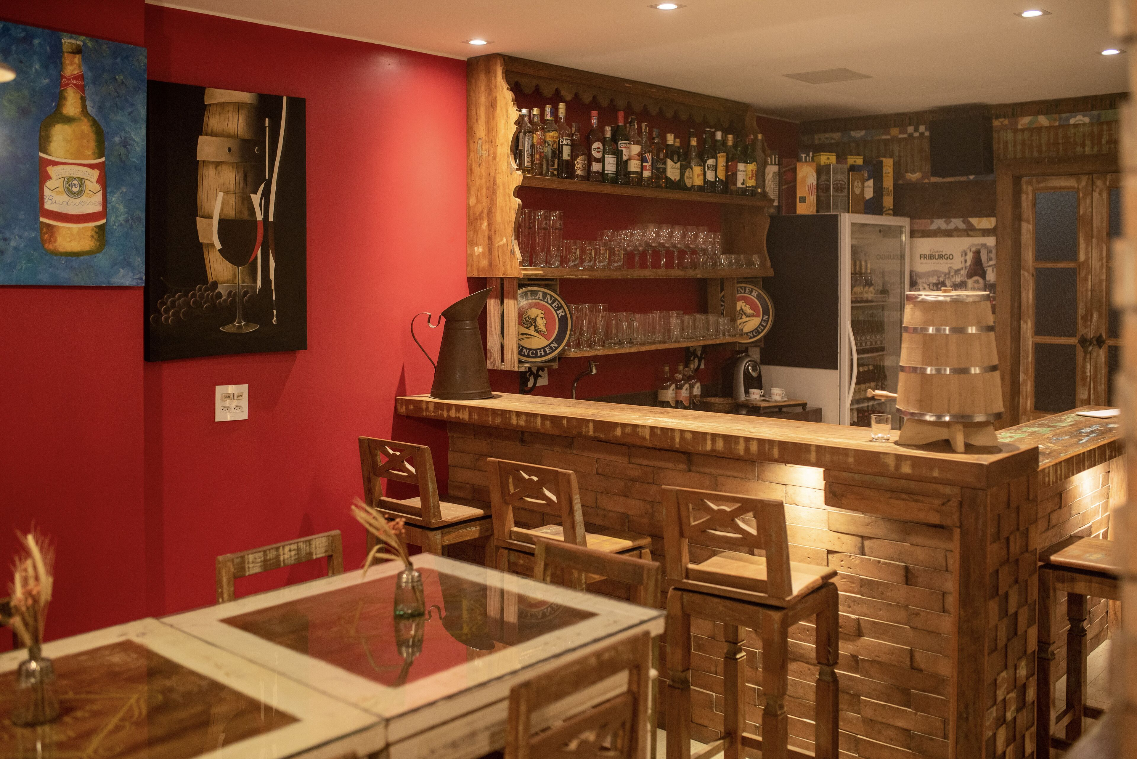 Eine Bar mit Holzkubeln, einer roten Wand und verschiedenen Flaschen und Gläsern auf Regalen.