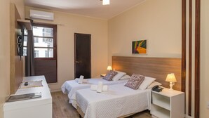 Habitación de hotel con dos camas, un escritorio, una silla, una mesita de noche con lámpara, aire acondicionado instalado en la pared y una ventana con cortinas.