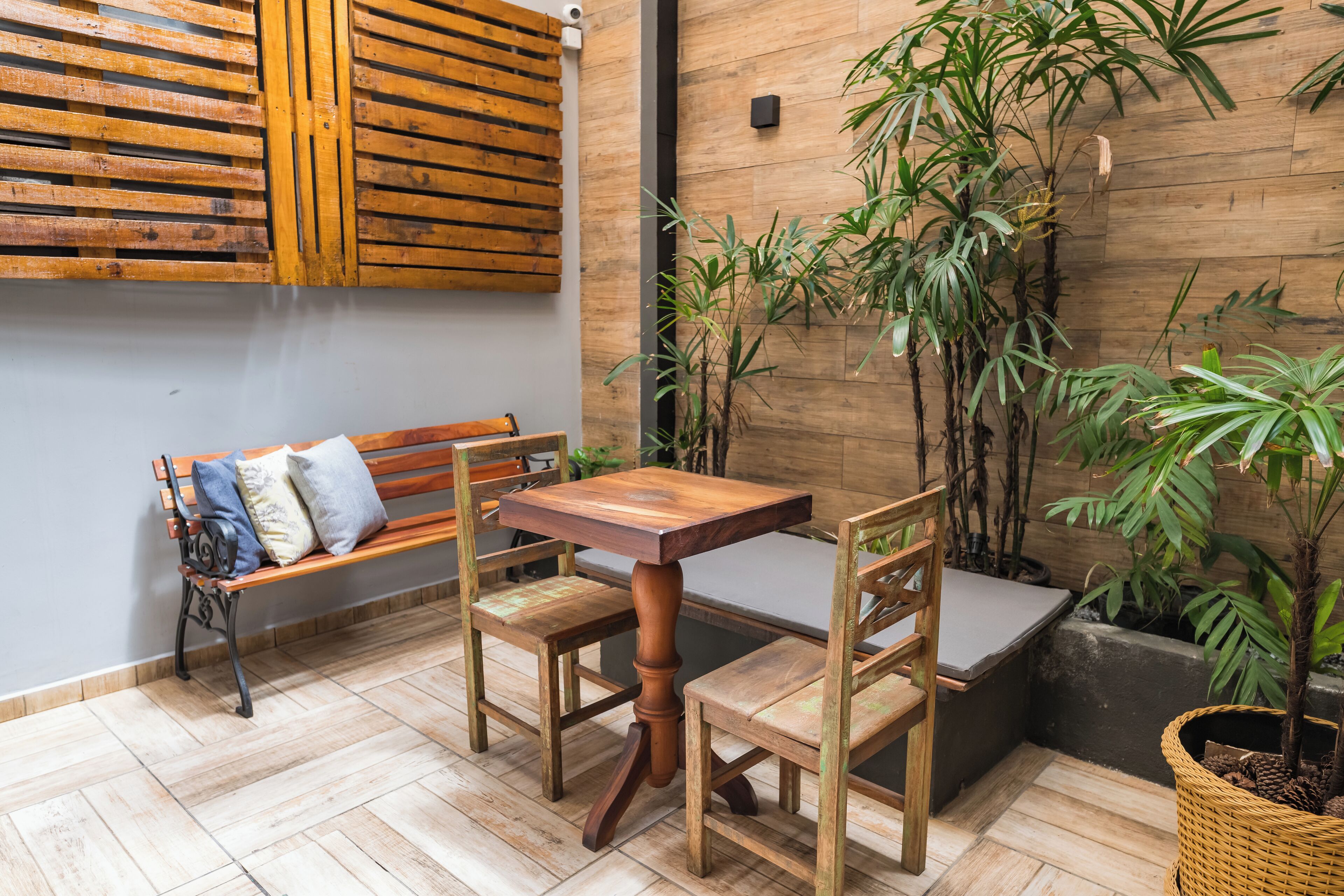 Une table et des chaises en bois se trouvent dans une pièce dont le sol est également en bois, et un banc agrémenté de coussins y est installé.