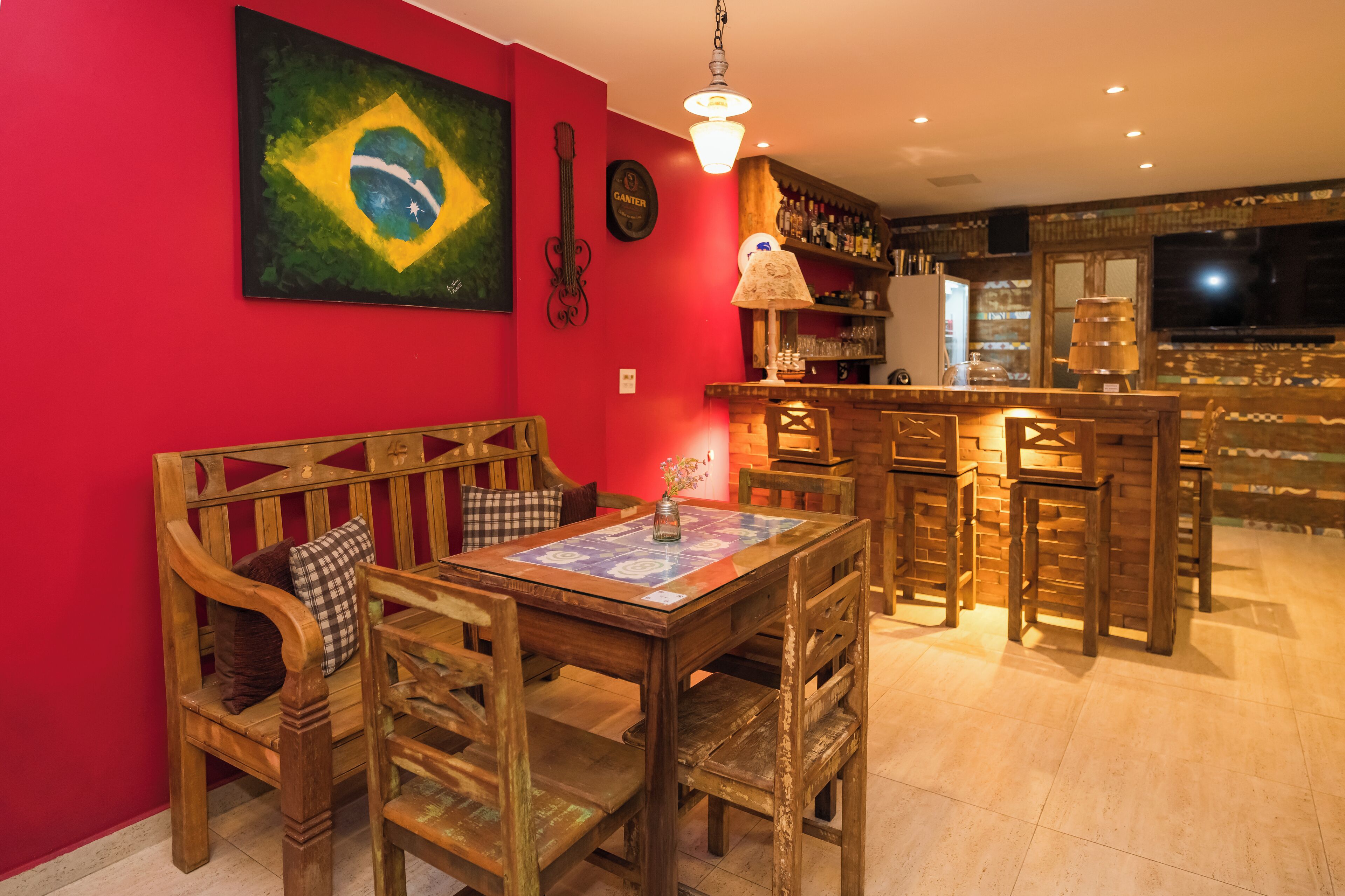 A room with a red wall, a wooden bench, a table with chairs, a bar area, and a television.