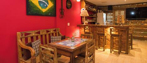 A room with a red wall, a wooden bench, a table with chairs, a bar area, and a television.