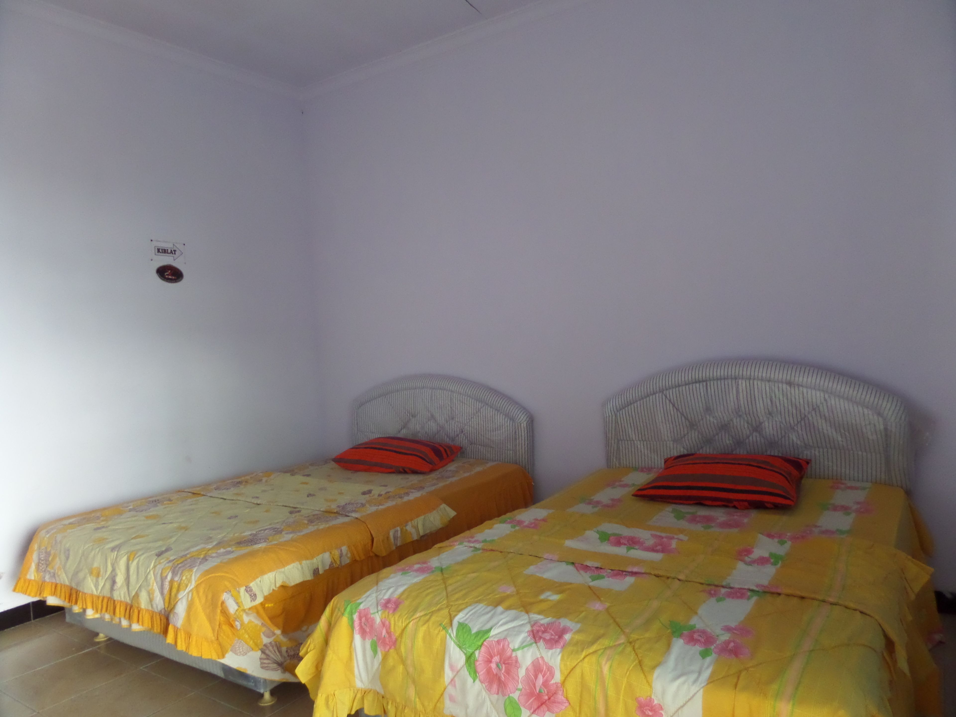Quarto pequeno e limpo com duas camas de solteiro, cada uma com colcha florida e travesseiro vermelho.