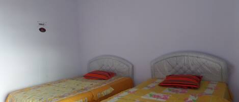 Quarto pequeno e limpo com duas camas de solteiro, cada uma com colcha florida e travesseiro vermelho.