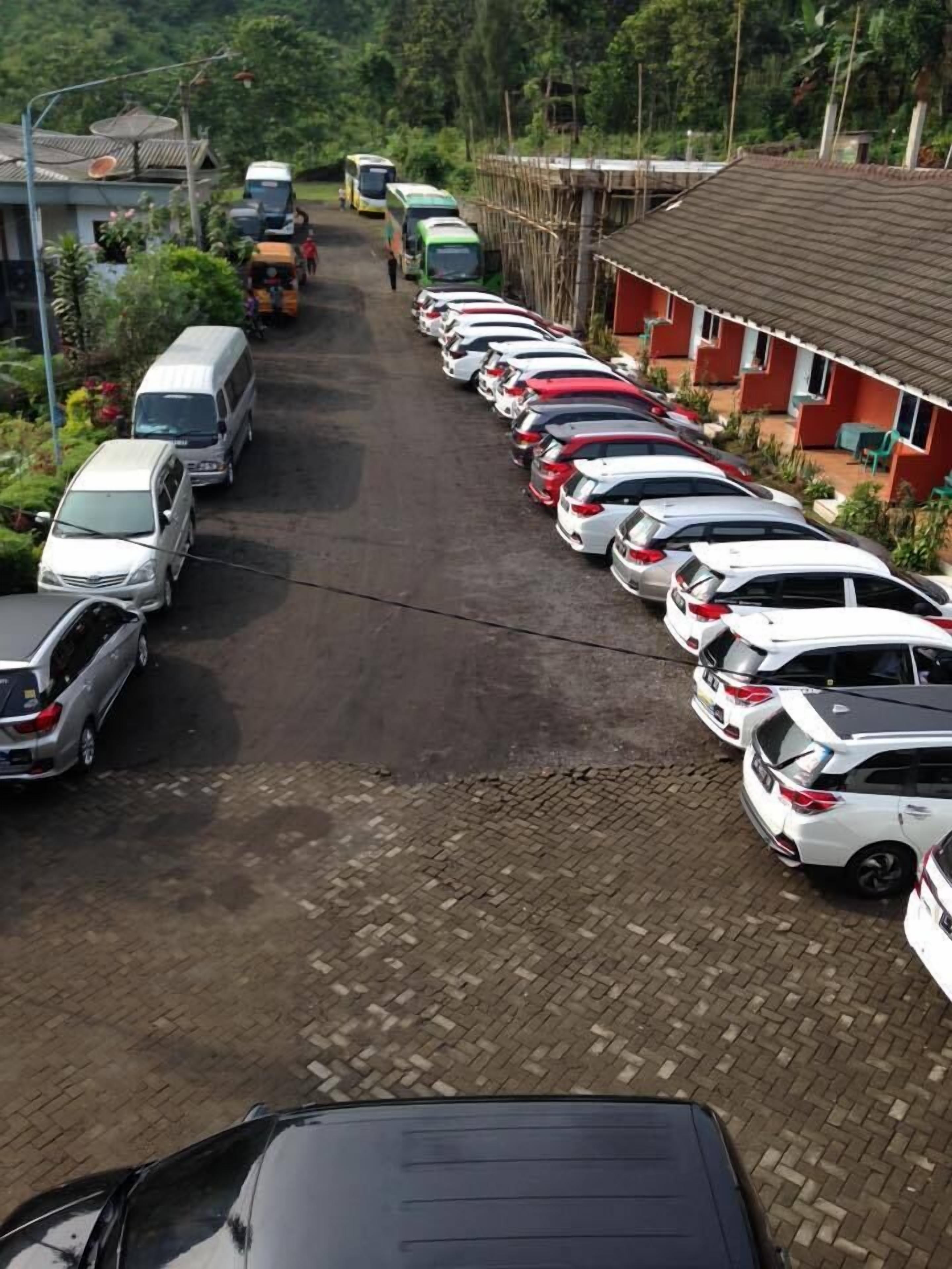 Een parkeerplaats met meerdere auto's en bussen, omringd door gebouwen en groen.