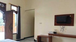 A hotel room with a bed, a TV mounted on the wall, a small wooden table, and a window with curtains. - Hotel Nadia Bromo (Sukapura)