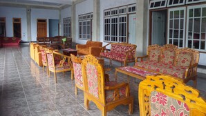 A spacious room with multiple wooden chairs and sofas arranged around a central table, large windows with white frames, and a tiled floor. - Hotel Nadia Bromo (Sukapura)