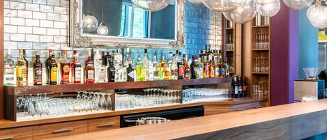 Zona de bar con espejo, estanterías llenas de botellas de licor y una variedad de vasos.