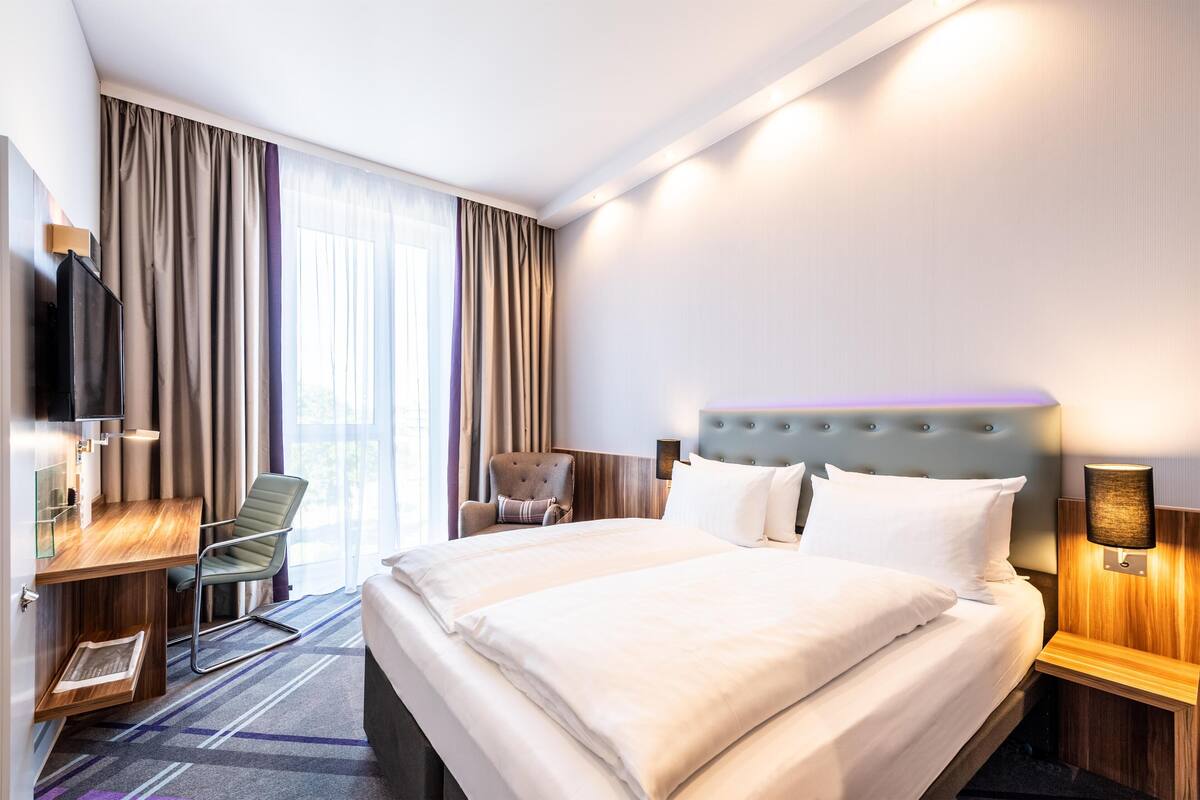 Ein Hotelzimmer mit einem großen Bett, einem Schreibtisch, einem Stuhl und einem Fernseher.