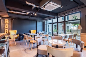 A modern bar area with seating, large windows, and a visible outdoor view.