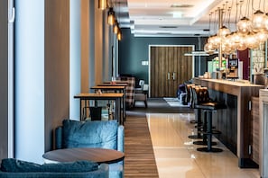 A modern bar area with high stools, a long counter, and pendant lighting.