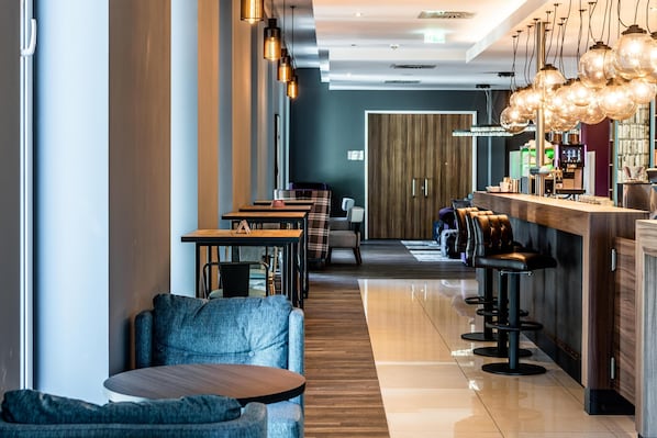 Zona de bar moderna amb tamborets alts, una barra llarga i il·luminació penjant.
