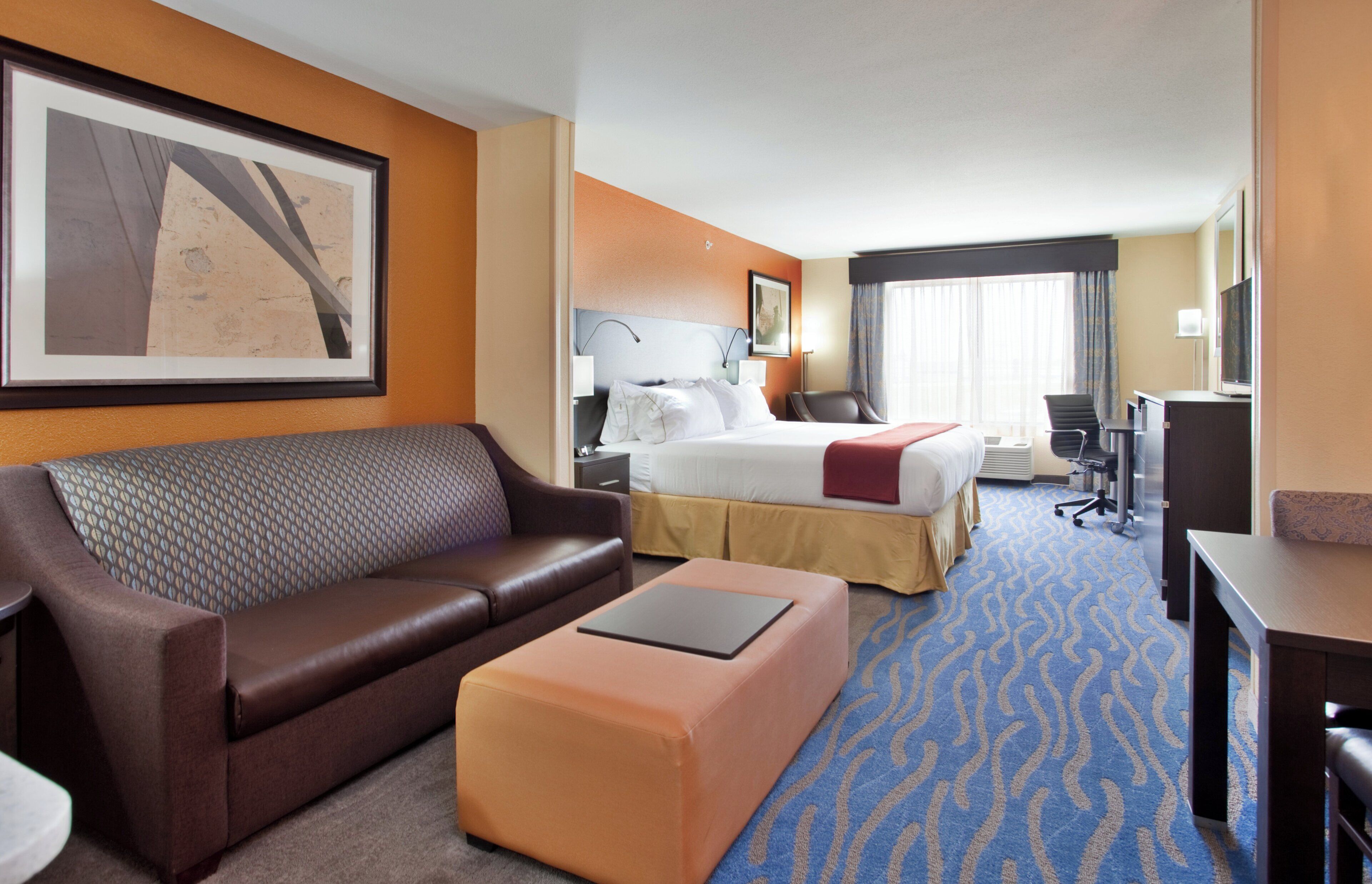 A hotel room with a sofa, a bed, a desk, and a large window.