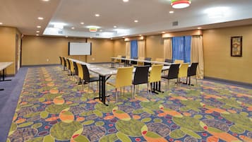A conference room with a long table, chairs, a projector screen, and a colorful carpet.